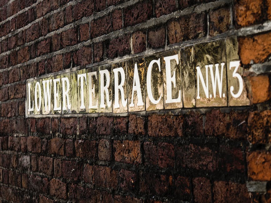 A close-up view of a red brick wall with a metal street sign that reads 'LOWER TERRACE NW3' in white letters on a green background. The sign is mounted on the left side of the image, with the brick su